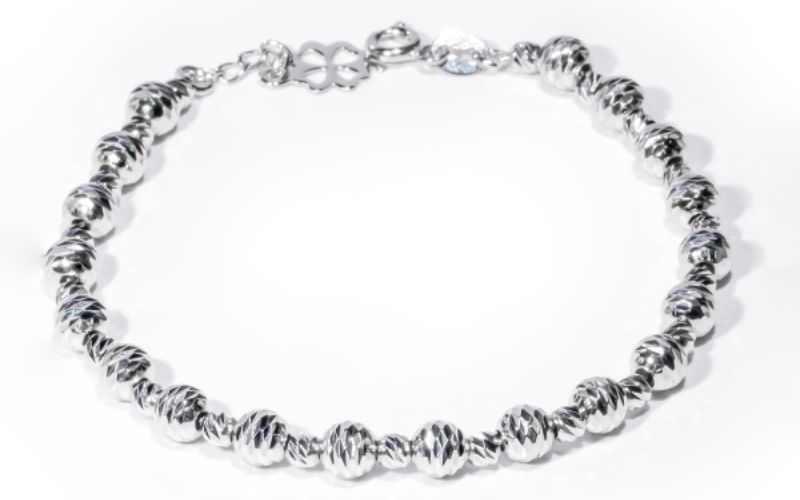 Hình ảnh mẫu Lắc Tay Vàng 18K Dưới 3 Triệu, chế tác từ vàng trắng au750, đang có chương trình giảm giá 8%. Lắc tay có thiết kế dạng chuỗi bi tròn đồng bộ, bề mặt mỗi bi được chạm khắc những đường vân tinh xảo giúp tăng độ bắt sáng và lấp lánh. Phần móc cài có dây nối dài được đính một charm cỏ bốn lá nhỏ nhắn.