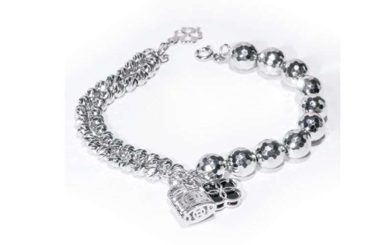 Hình ảnh một mẫu Lắc Tay Vàng 18K Dưới 3 Triệu có thiết kế độc đáo và cá tính. Được chế tác từ vàng trắng au750, chiếc lắc tay kết hợp hai phong cách khác biệt: một nửa là chuỗi bi tròn to, sáng bóng và được cắt giác tinh tế, nửa còn lại là chuỗi xích kép thanh mảnh. Điểm nhấn của sản phẩm là các charm treo trang trí, bao gồm một charm hình trái tim có họa tiết và một charm hình khác, tạo nên vẻ ngoài thời trang và lạ mắt.