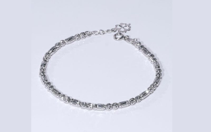 Một chiếc Lắc Tay Vàng 18K Dưới 3 Triệu với kiểu dáng thanh lịch và hiện đại, được làm từ vàng trắng au750. Thiết kế của lắc tay là một chuỗi mắt xích xen kẽ giữa các đốt hình trụ dài và các bi tròn nhỏ được cắt giác tinh xảo, tạo hiệu ứng lấp lánh. Phần dây nối dài có gắn một charm cỏ bốn lá nhỏ xinh, tượng trưng cho sự may mắn.